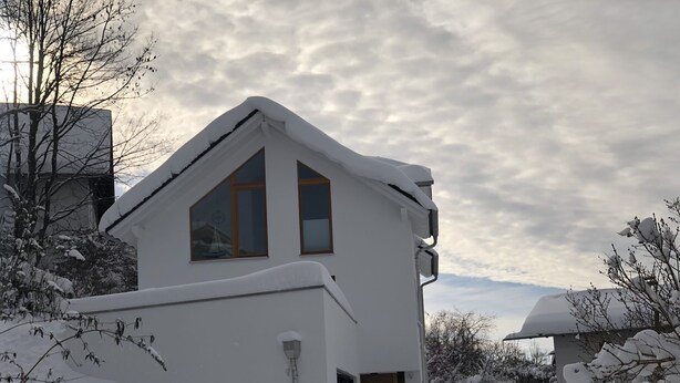 A snow-covered house with a triangular roof, a visible chimney, and a window with a sailboat decoration.