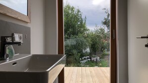 Een badkamer met een houten terras, een wastafel en uitzicht op een tuin met bomen en een hek.
