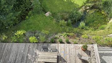 A wooden deck with a table and chairs, surrounded by a lush garden with various plants and a small pond.