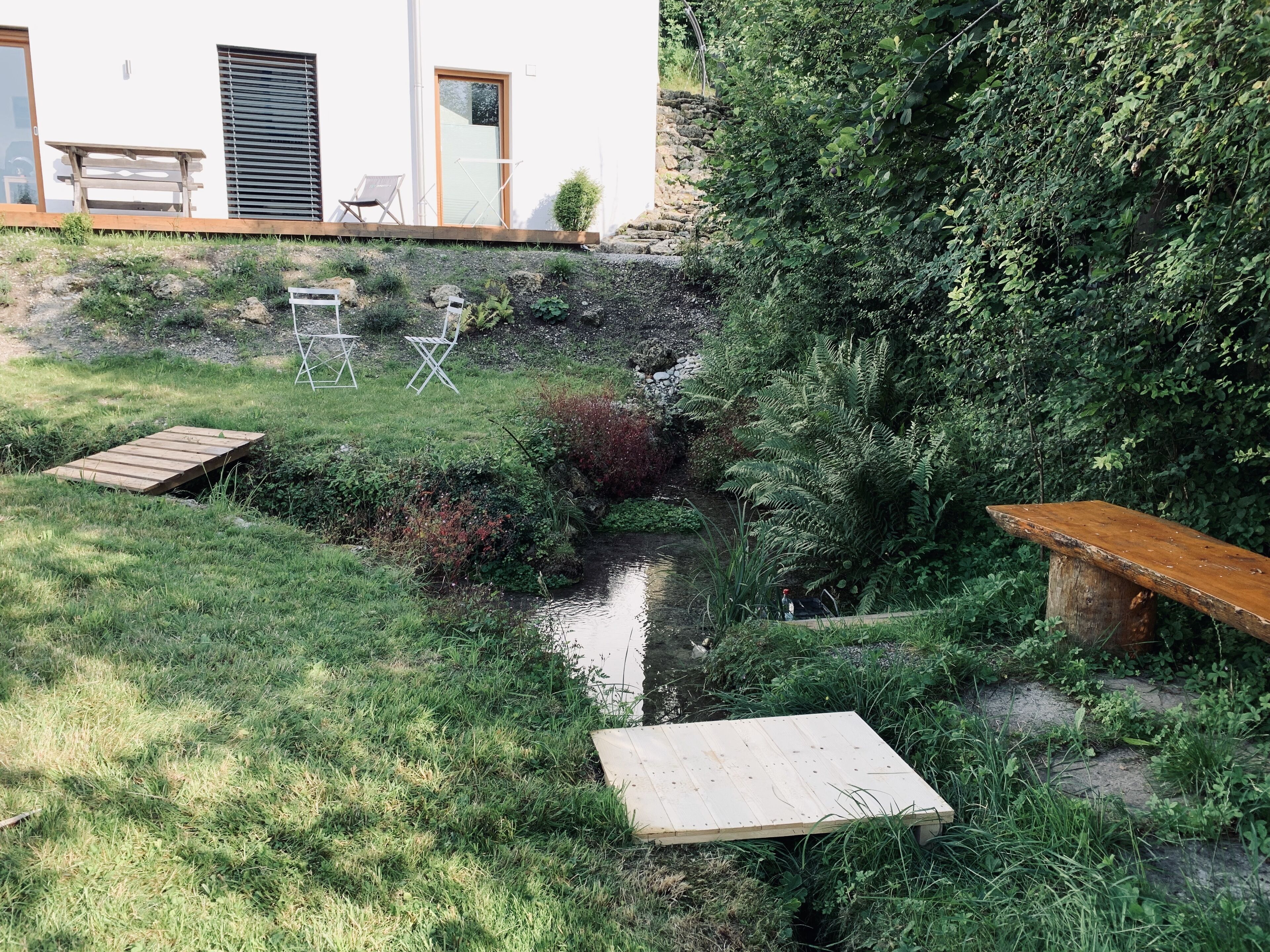 A garden with a small stream, wooden benches, and outdoor furniture.