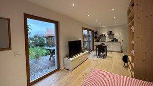 Een modern appartement met een grote schuifpui naar een balkon, een keuken met witte kastjes en een eethoek met een rood-wit geruit tafelkleed.