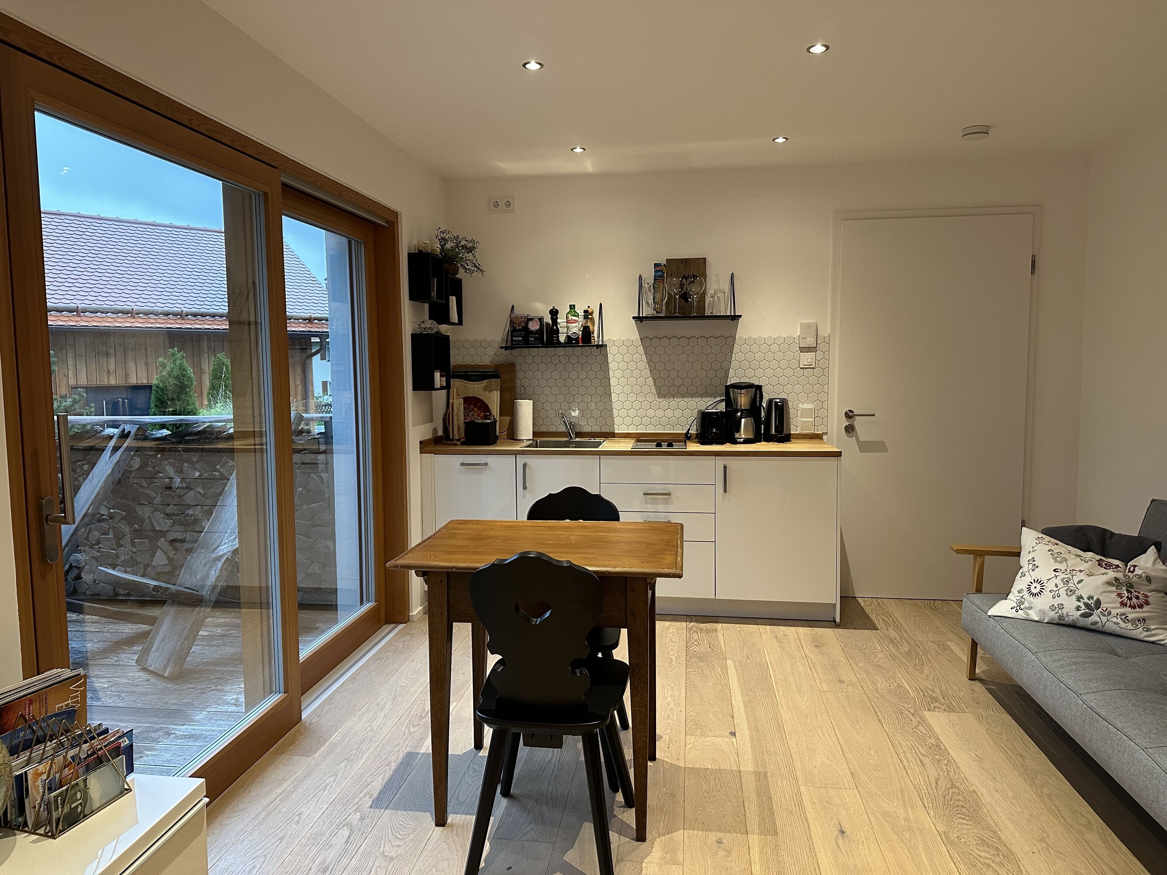 A modern kitchen with a dining area, a sofa, and a view of the outside.