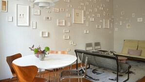 A modern living room with a round dining table, two chairs, a sofa, and a coffee table. The walls are adorned with numerous framed artworks.