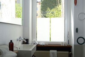 Une salle de bain avec une fenêtre, un lavabo, un miroir et un porte-serviettes.