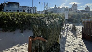 A beach with a large woven structure, a sandy path, and buildings in the background.