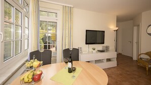 A dining area with a table set for two, a TV mounted on the wall, and a view of the outdoors through large windows.