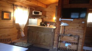 A wooden cabin interior with a kitchenette, a microwave, a television, and a small table with a lamp.