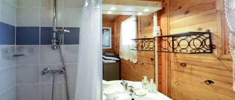 A wooden cabin bathroom with a shower, sink, and mirror.