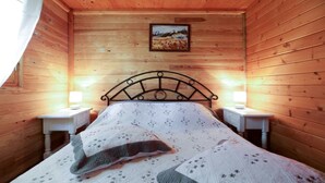 A cozy wooden room with a bed, two bedside lamps, and a painting on the wall.