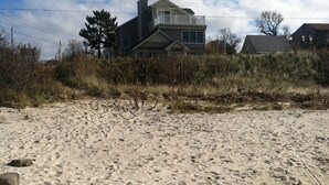 Una casa frente a la playa con balcón, rodeada de arena y vegetación.