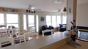 Amplia sala de estar con una mesa de comedor, sillas blancas, un sofá azul y una zona de cocina con cafetera.
