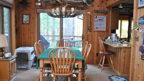 L’intérieur d’un chalet en bois comprend une table à manger, des chaises, une cheminée, une niche pour animaux de compagnie et une pancarte sur laquelle on peut lire : « MANGER, DORMIR, CHASSER ».