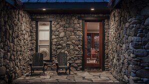 Fachada de piedra con dos sillas Adirondack y una puerta de entrada.