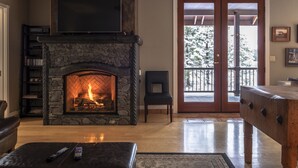 Un salón con chimenea de piedra, un televisor montado encima y una mesa de centro de madera.