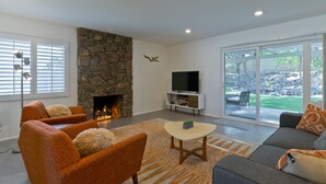Ein modernes Wohnzimmer mit Kamin aus Stein, orangefarbenen Sesseln, einem grauen Sofa und einem großen Fernseher.