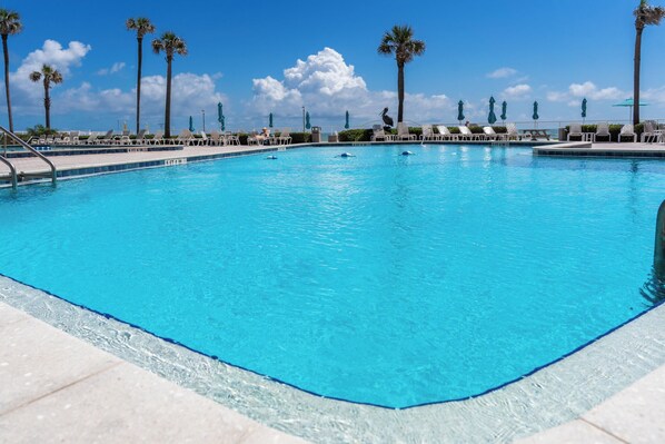 A clear blue pool with lounge chairs and palm trees in the background.