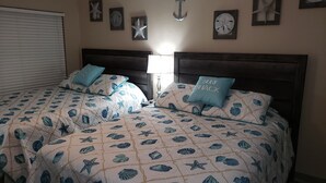 A bedroom with two beds, each with a headboard, a window with blinds, and wall decorations including starfish and an anchor. - FUN VACATION GETAWAY (South Padre Island)