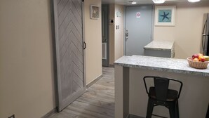 A kitchen with a sliding door, a small island with a basket of fruit, and a chair. - FUN VACATION GETAWAY (South Padre Island)