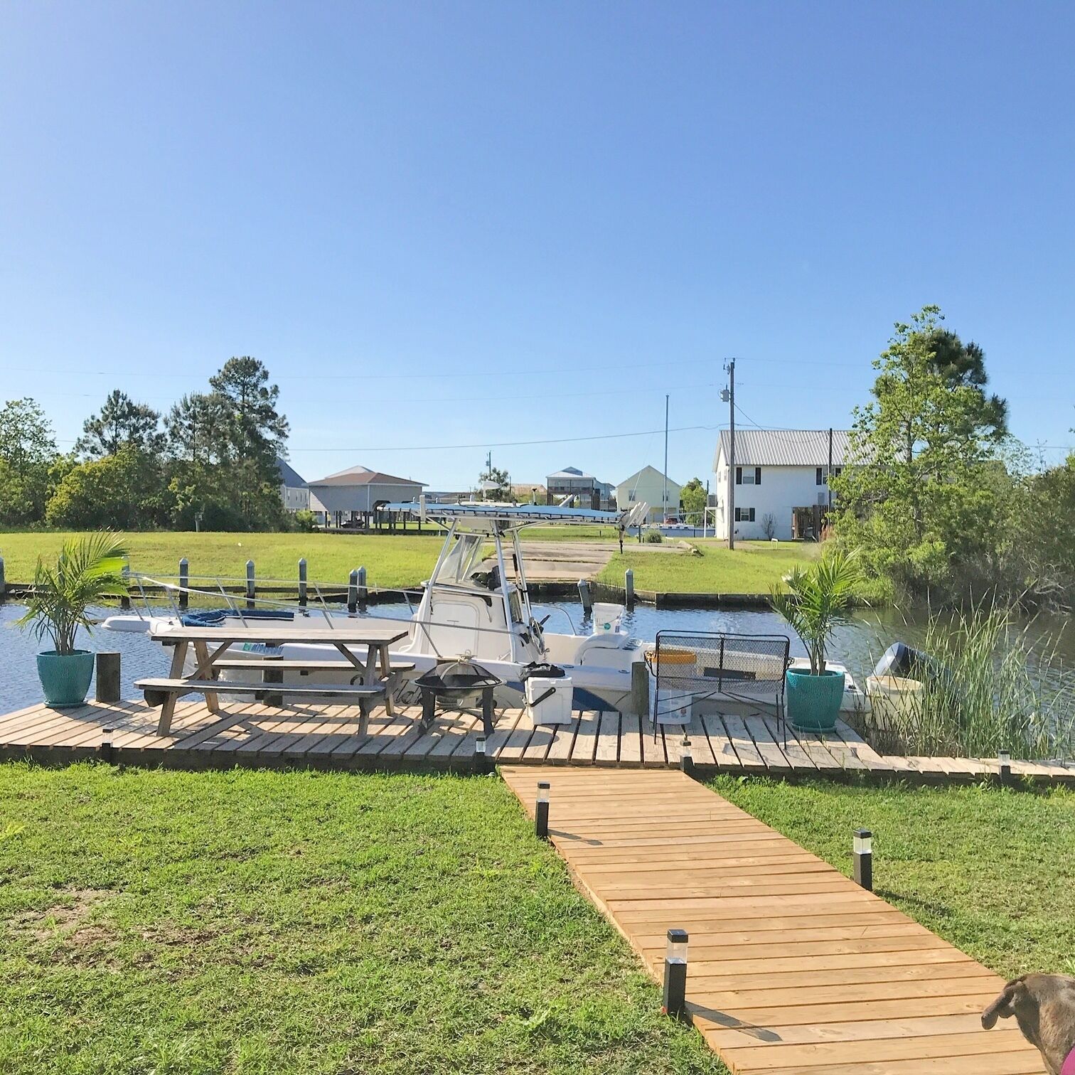 Un port de plaisance avec des bateaux amarrés, une promenade en bois et une zone herbeuse agrémentée de plantes en pot.