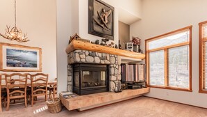 A cozy living room with a stone fireplace, wooden mantel, and a dining area with chairs and a table.