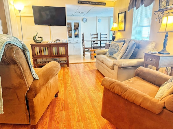 A living room with a sofa, armchair, wooden floor, TV, lamp, and a cabinet.