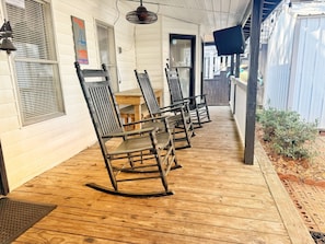 A porch with rocking chairs, a wooden table, and a covered area with a fan.