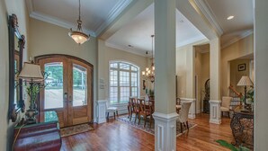A spacious foyer with a wooden floor, a grand staircase, and a dining area with a chandelier.