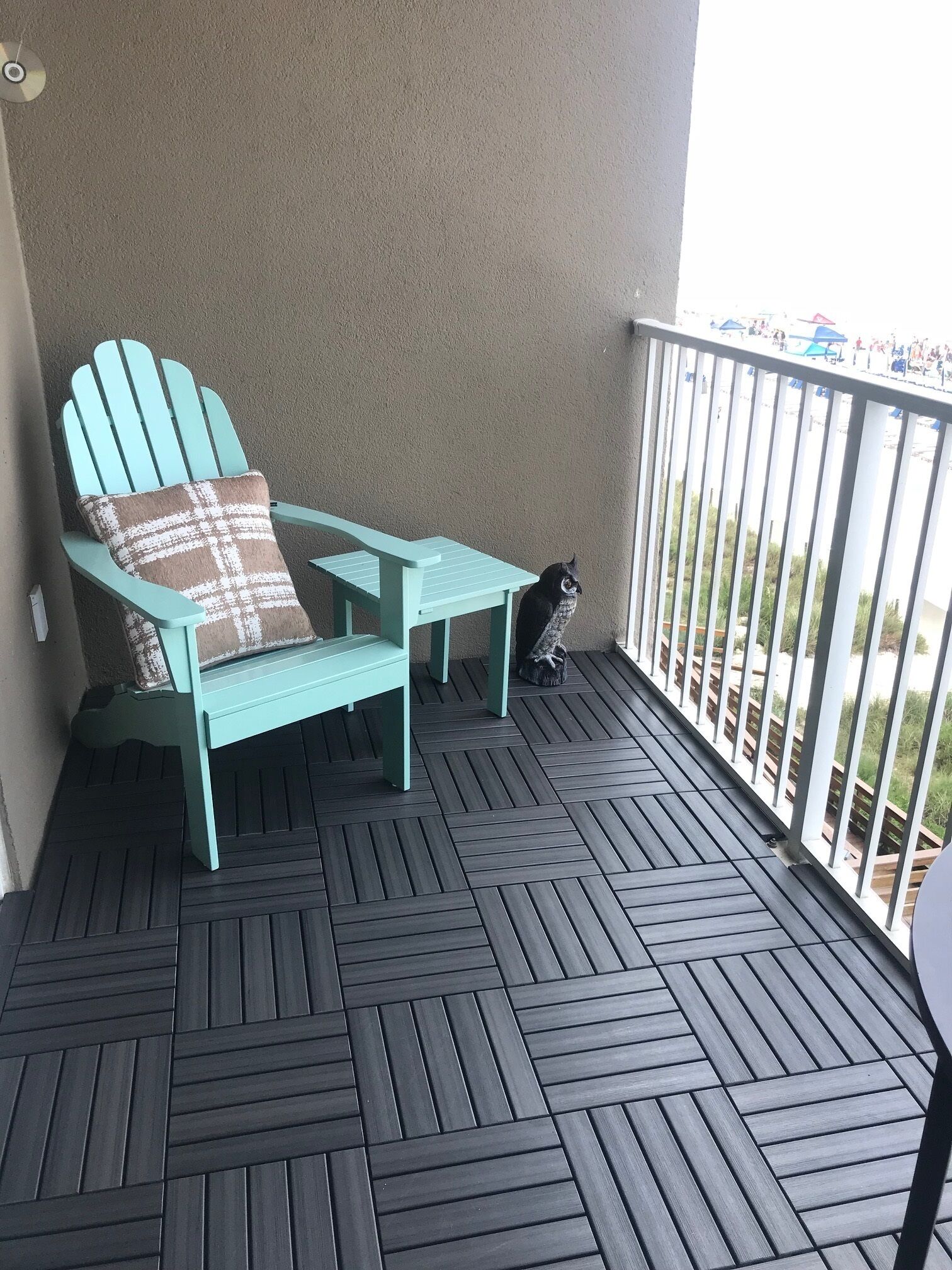 Ein türkisfarbener Adirondack-Stuhl mit kariertem Kissen auf einem Balkon mit dunklem Holzboden.