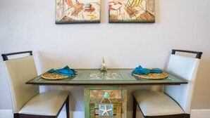 A dining area with a glass table, two chairs, and a view of the beach through open shutters. - Spectacular -  Beach front condo from 149 night - no extra administrative fees. (Panama City Beach)