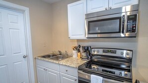 Une cuisine avec des armoires blanches, un évier à deux bacs, un four à micro-ondes et une cuisinière.