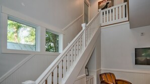 A staircase with white railings and a wooden handrail, leading to a landing with a framed picture and a leather chair. - Live oak views from this 3 bedroom cottage; 2 golf carts and peaceful screened in porch (Bald Head Island)