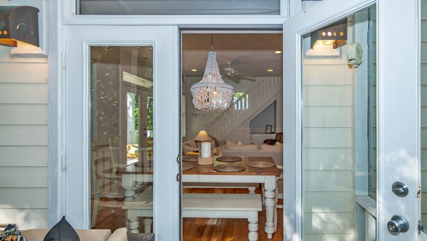 A dining area with a chandelier, a table set with plates and a pitcher, and a staircase leading upstairs. - Live oak views from this 3 bedroom cottage; 2 golf carts and peaceful screened in porch (Bald Head Island)