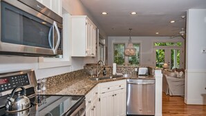 A modern kitchen with stainless steel appliances, granite countertops, and white cabinetry. - Live oak views from this 3 bedroom cottage; 2 golf carts and peaceful screened in porch (Bald Head Island)