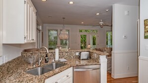 A kitchen with granite countertops, stainless steel appliances, and a view to a dining area. - Live oak views from this 3 bedroom cottage; 2 golf carts and peaceful screened in porch (Bald Head Island)
