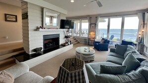 A spacious living room with a fireplace, comfortable seating, and large windows offering ocean views. - Waterfront w/ New Saltwater Heated Pool, Private Pier and Basketball Hoop. (Morehead City)