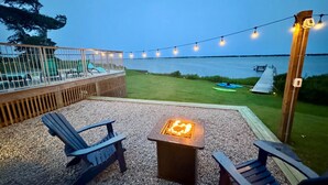 An outdoor patio with Adirondack chairs, a square fire pit, and string lights. - Waterfront w/ New Saltwater Heated Pool, Private Pier and Basketball Hoop. (Morehead City)