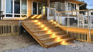 A wooden deck with steps leading to a covered area with railings. - Waterfront w/ New Saltwater Heated Pool, Private Pier and Basketball Hoop. (Morehead City)