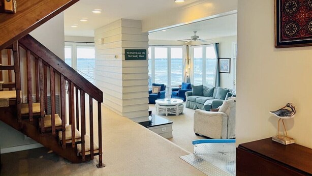 A modern interior with a wooden staircase leading to a living area with a view of the ocean. - Waterfront w/ New Saltwater Heated Pool, Private Pier and Basketball Hoop. (Morehead City)
