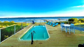 A wooden deck with a pool, lounge chairs, and a table overlooking the ocean. - Waterfront w/ New Saltwater Heated Pool, Private Pier and Basketball Hoop. (Morehead City)