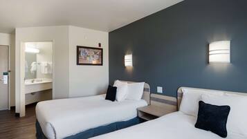 Quarto de hotel com duas camas, banheiro e uma pequena mesa.
