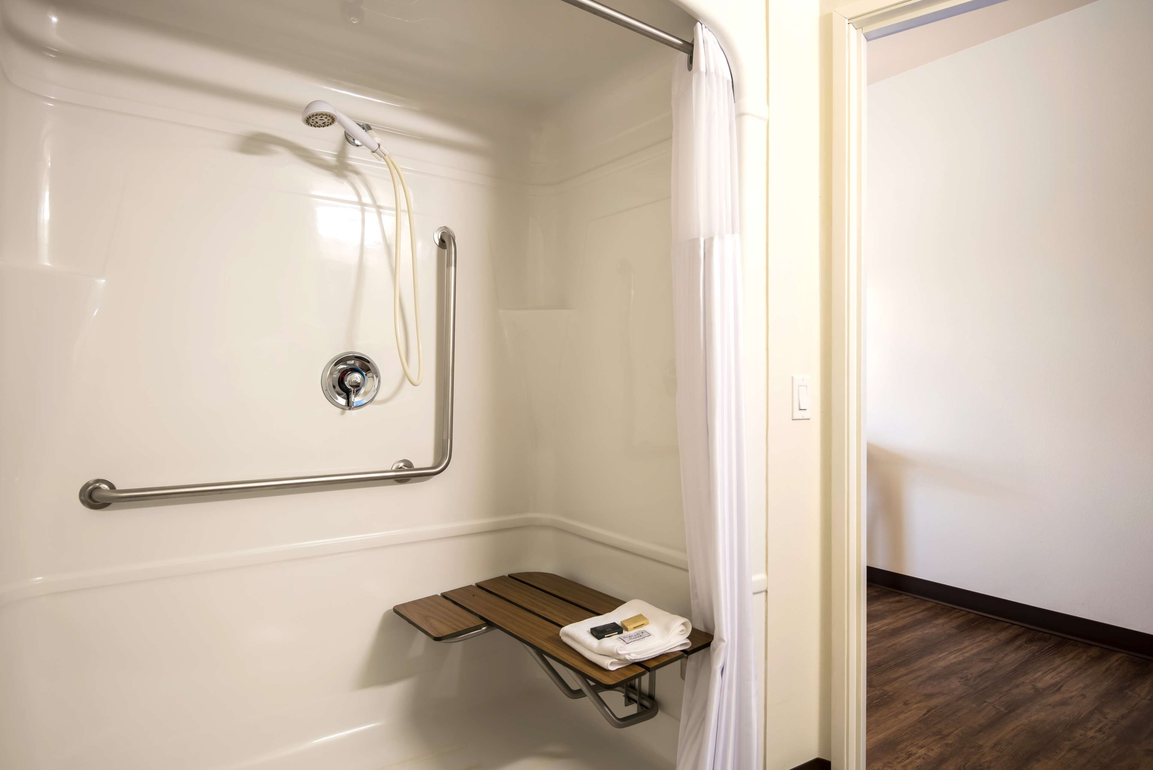 A shower area with a grab bar, a shelf with toiletries, and a showerhead.