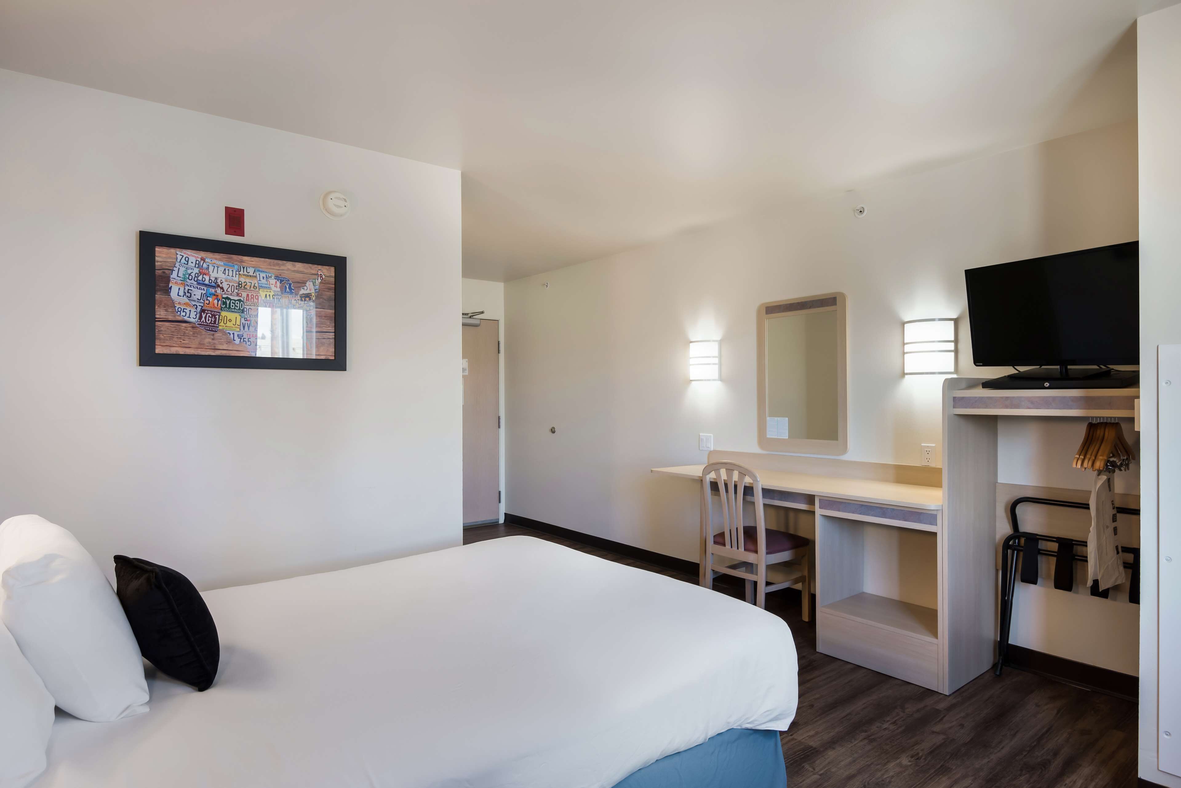 Una habitación de hotel con cama, escritorio, silla, televisor y espejo.