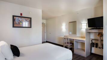 Una habitación de hotel con cama, escritorio, silla, televisor y espejo.