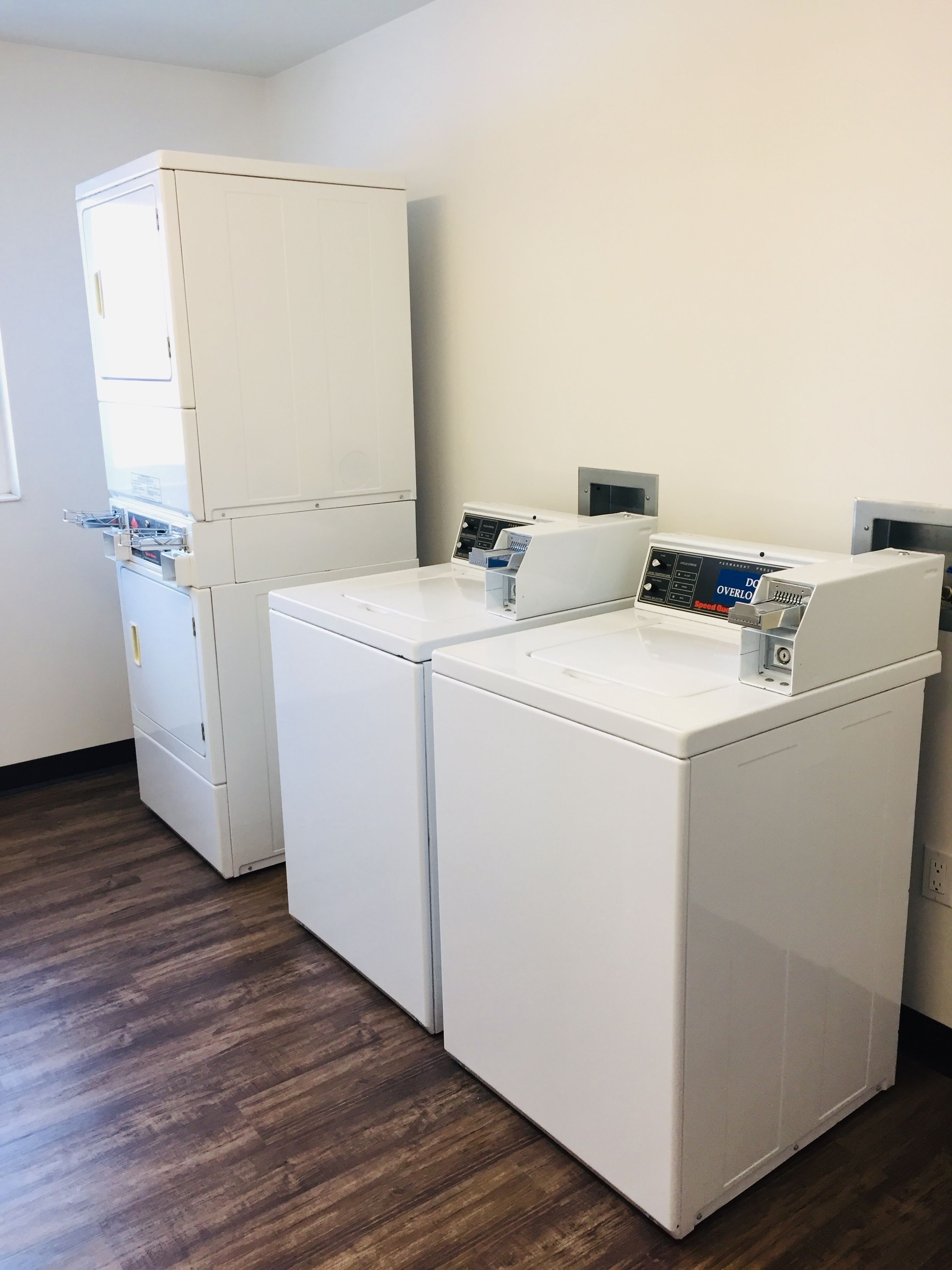 A laundry room with two front-loading washing machines and a stacked dryer.