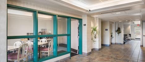 A hotel lobby with a tiled floor, a reception desk, and a seating area with chairs and tables.