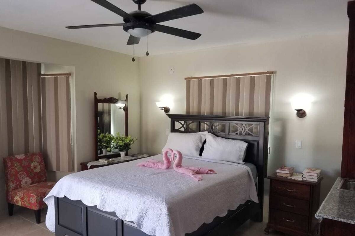 A bedroom with a bed, a nightstand, a chair, a ceiling fan, and a bedside table.