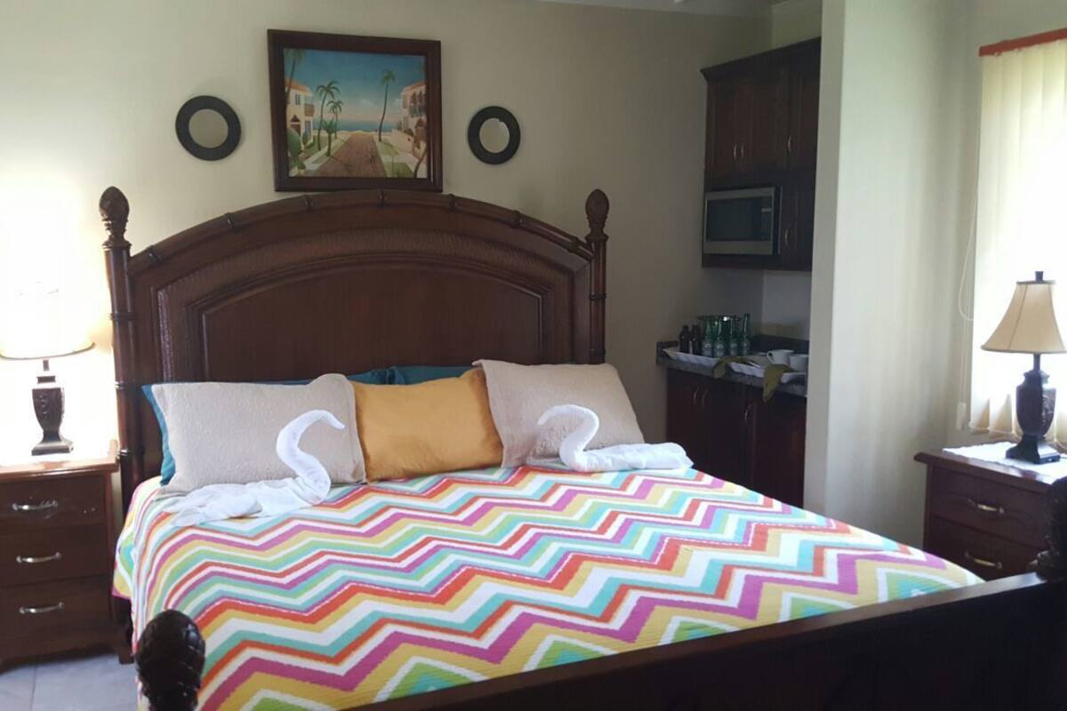 A neatly made bed with a colorful zigzag bedspread, a wooden headboard, and two bedside lamps.