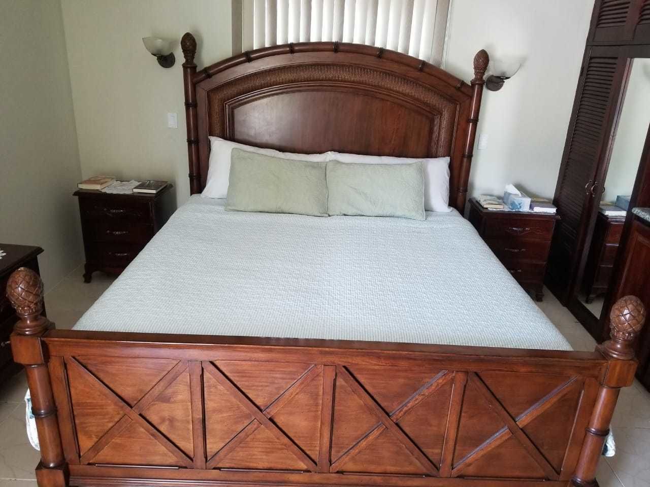 Una cama de madera con cabecera, dos mesitas de noche y un espejo a la derecha.