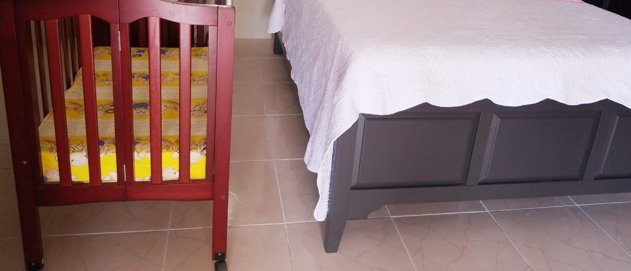 A room with a bed, a crib, and tiled flooring.