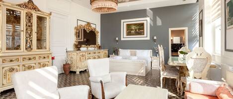 A room with a large ornate cabinet, a bed with white linens, a chandelier, and a painting on the wall.